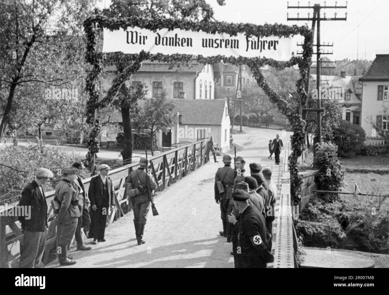 Occupation of the Sudetenland, with German and Czech border guards standing on the bridge which forms the new border. A sign above says (in German) 'We thank our Fuehrer' (Adolf Hitler). Stock Photo