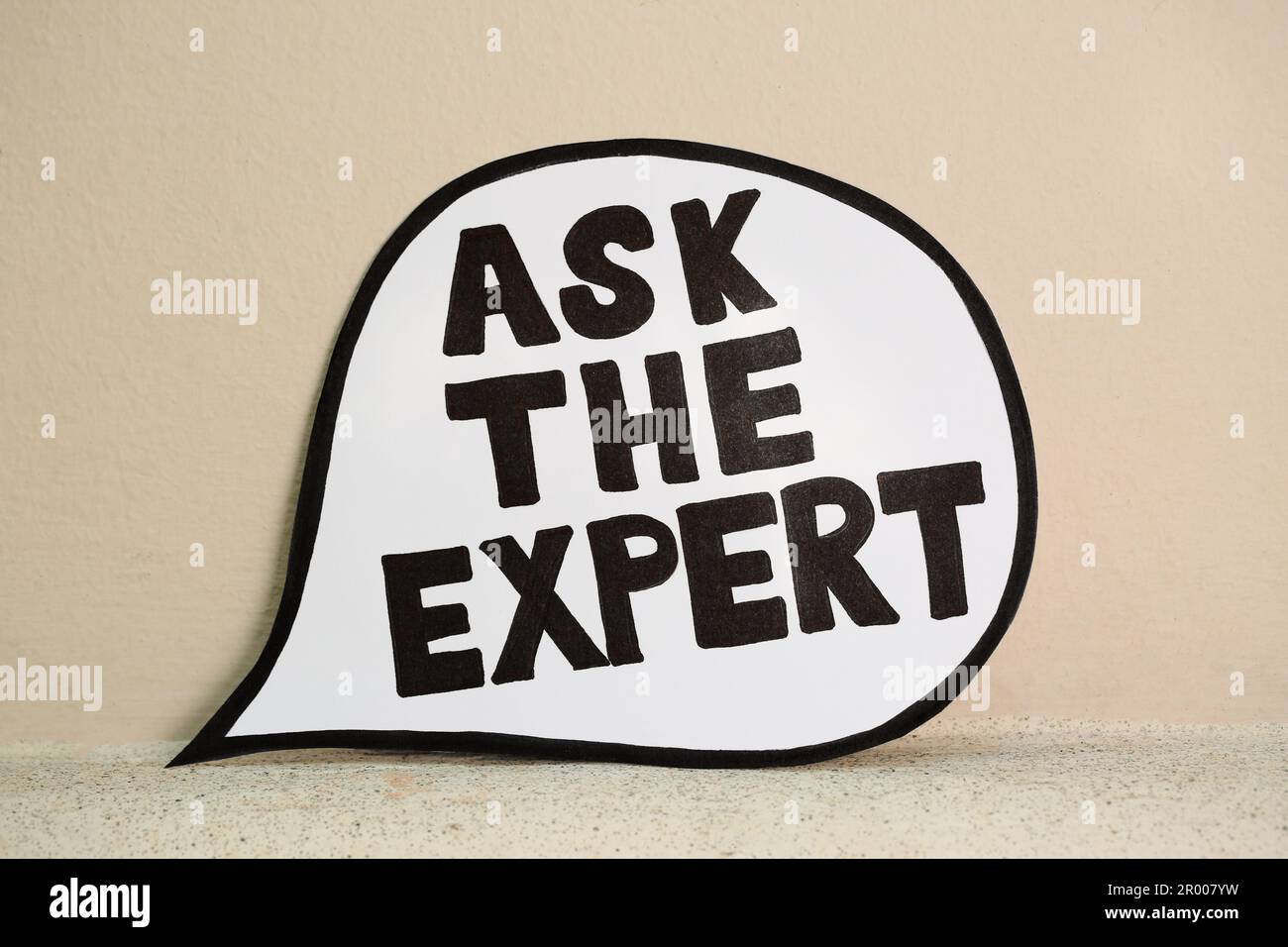 Paper message bubble with phrase Ask The Expert near beige wall Stock Photo