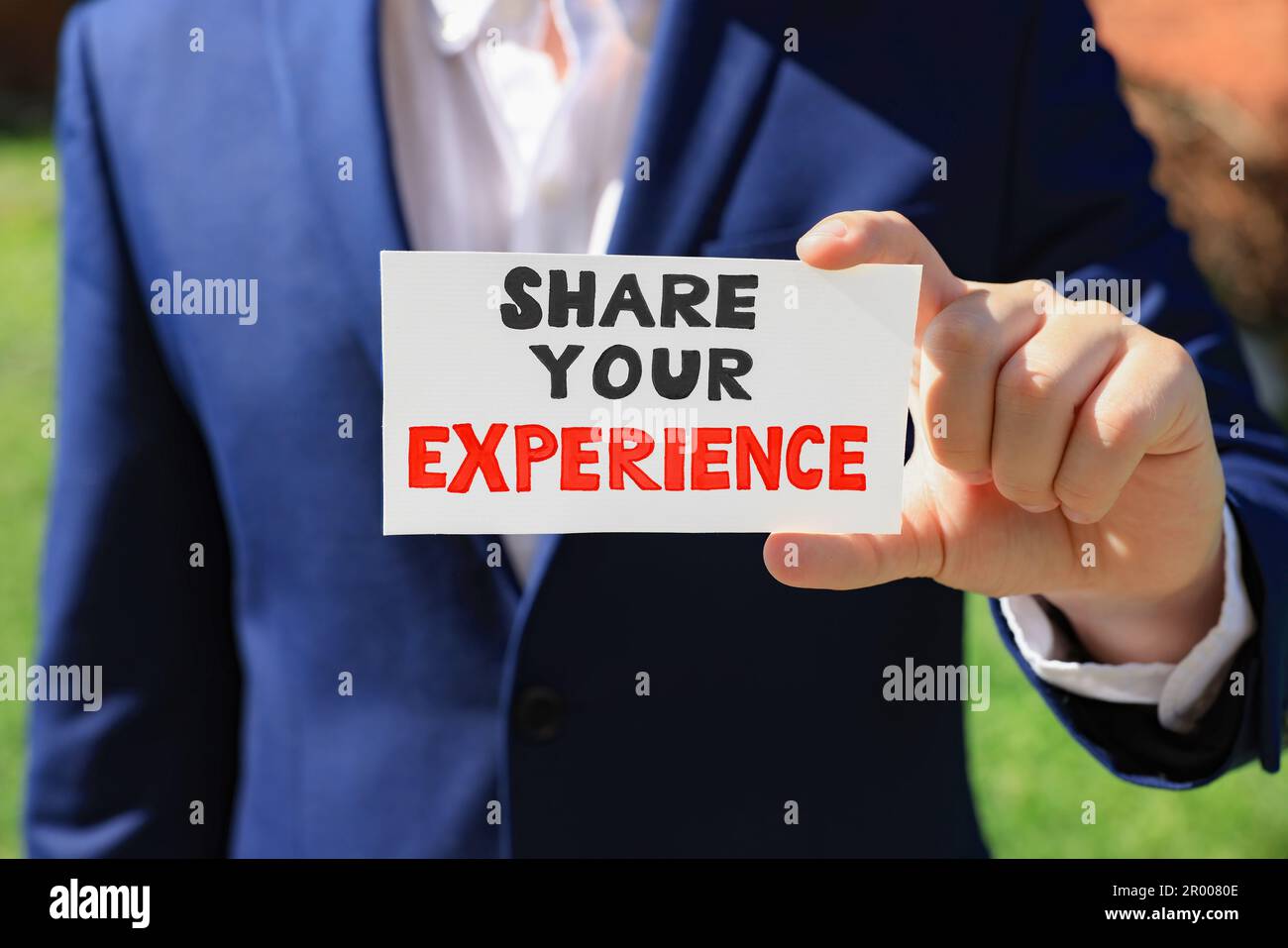 Man holding card with phrase Share Your Experience outdoors, closeup Stock Photo