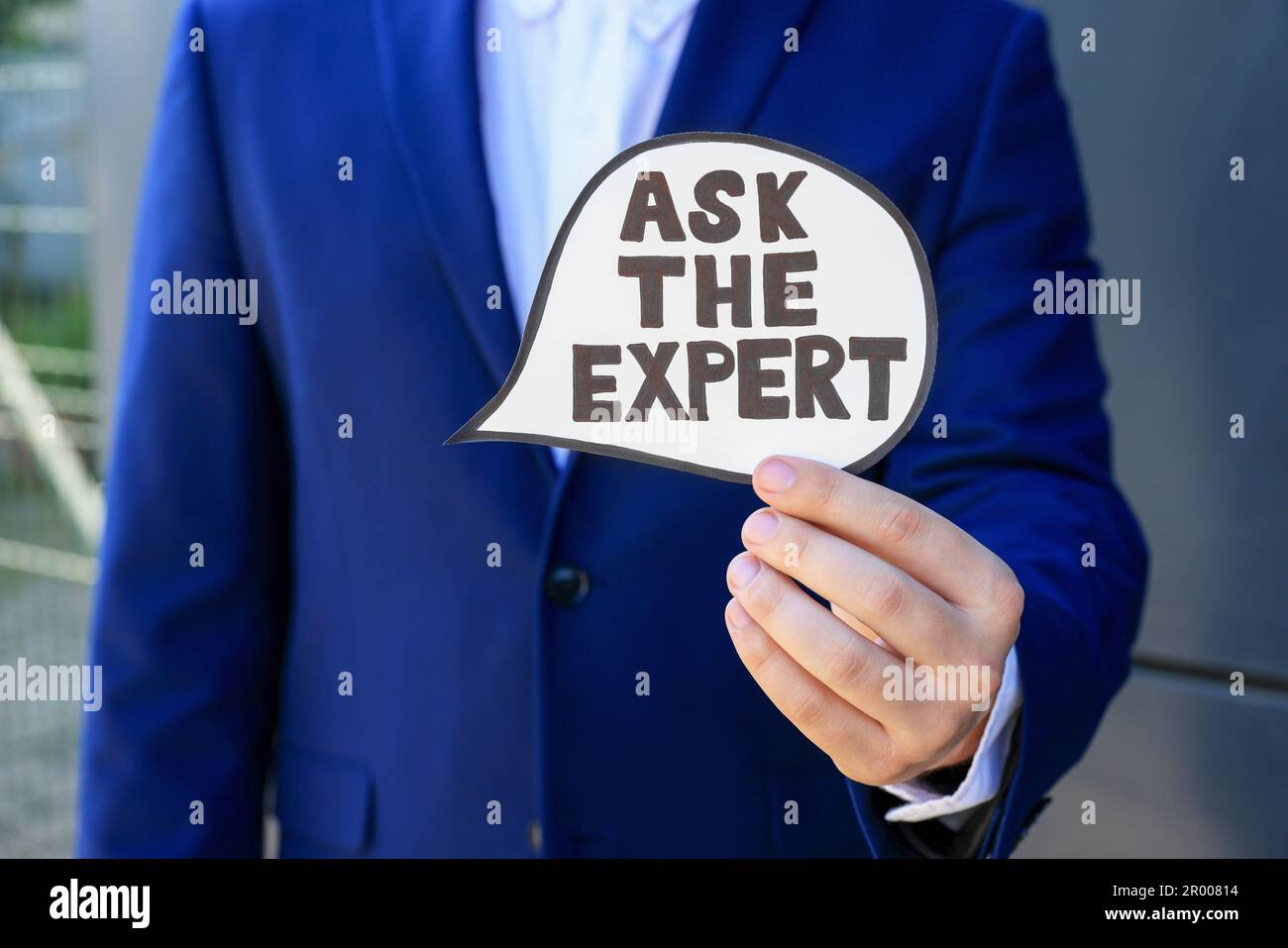 Man holding card with phrase Ask The Expert near black wall, closeup Stock Photo