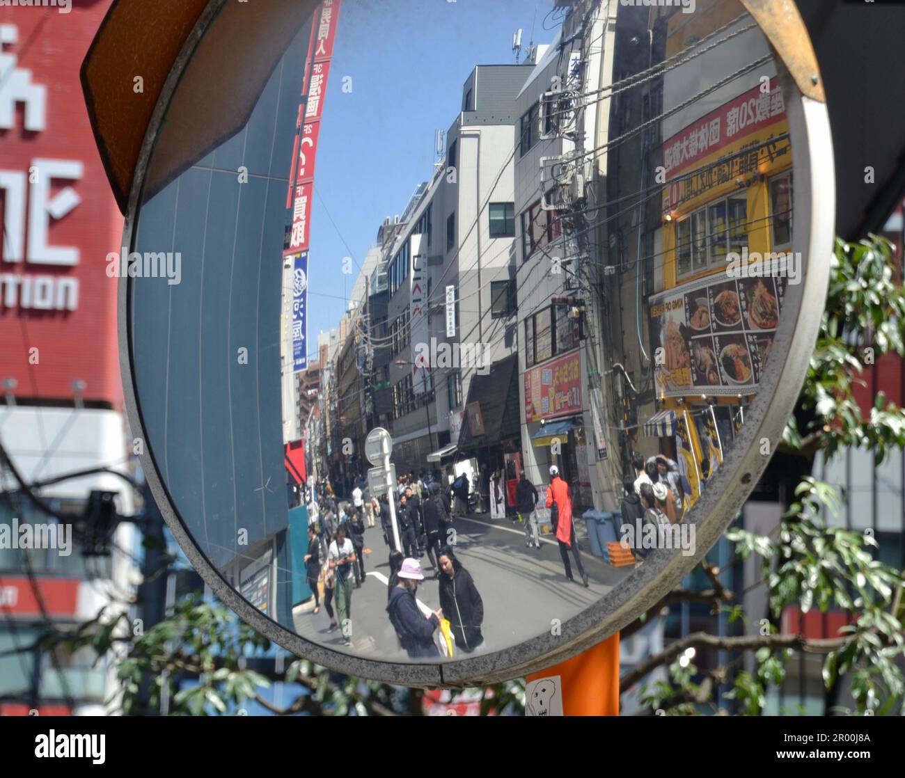 Restaurant and shopping strip street in Sendai Japan as reflected in a convex safety mirror at a road intersection has pedestrians, advertising signs Stock Photo