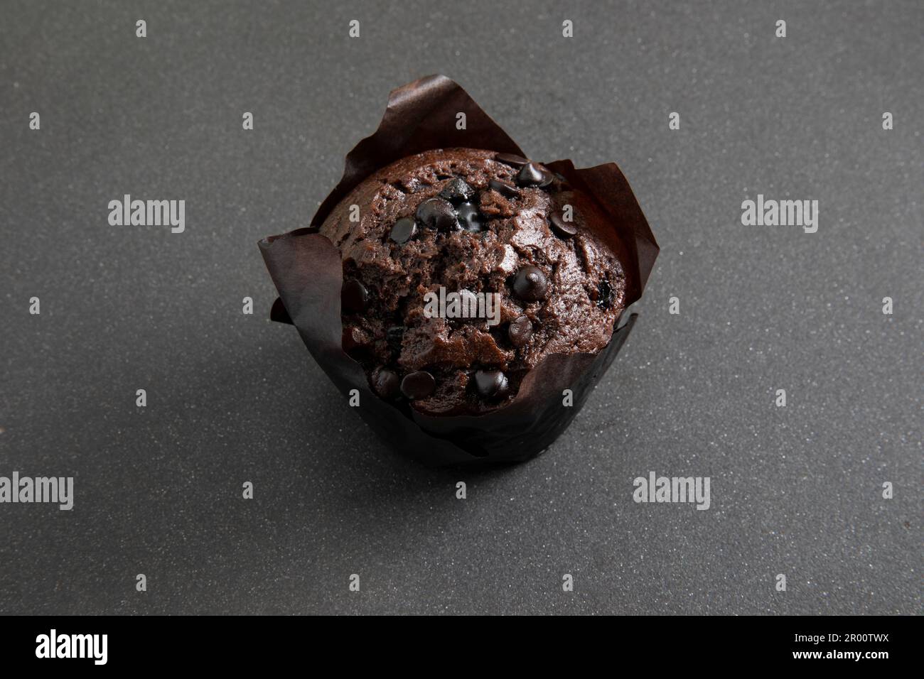Chocolate muffin in brown paper cup with chocolate pieces on black background Stock Photo