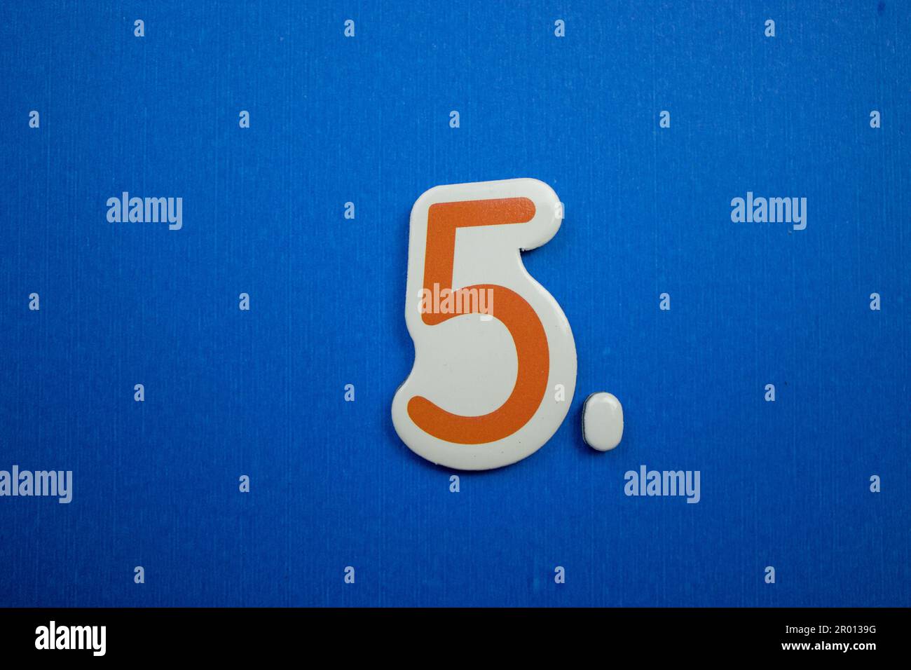 The number 5, placed on a blue background, photographed from above, colored orange and white. Stock Photo