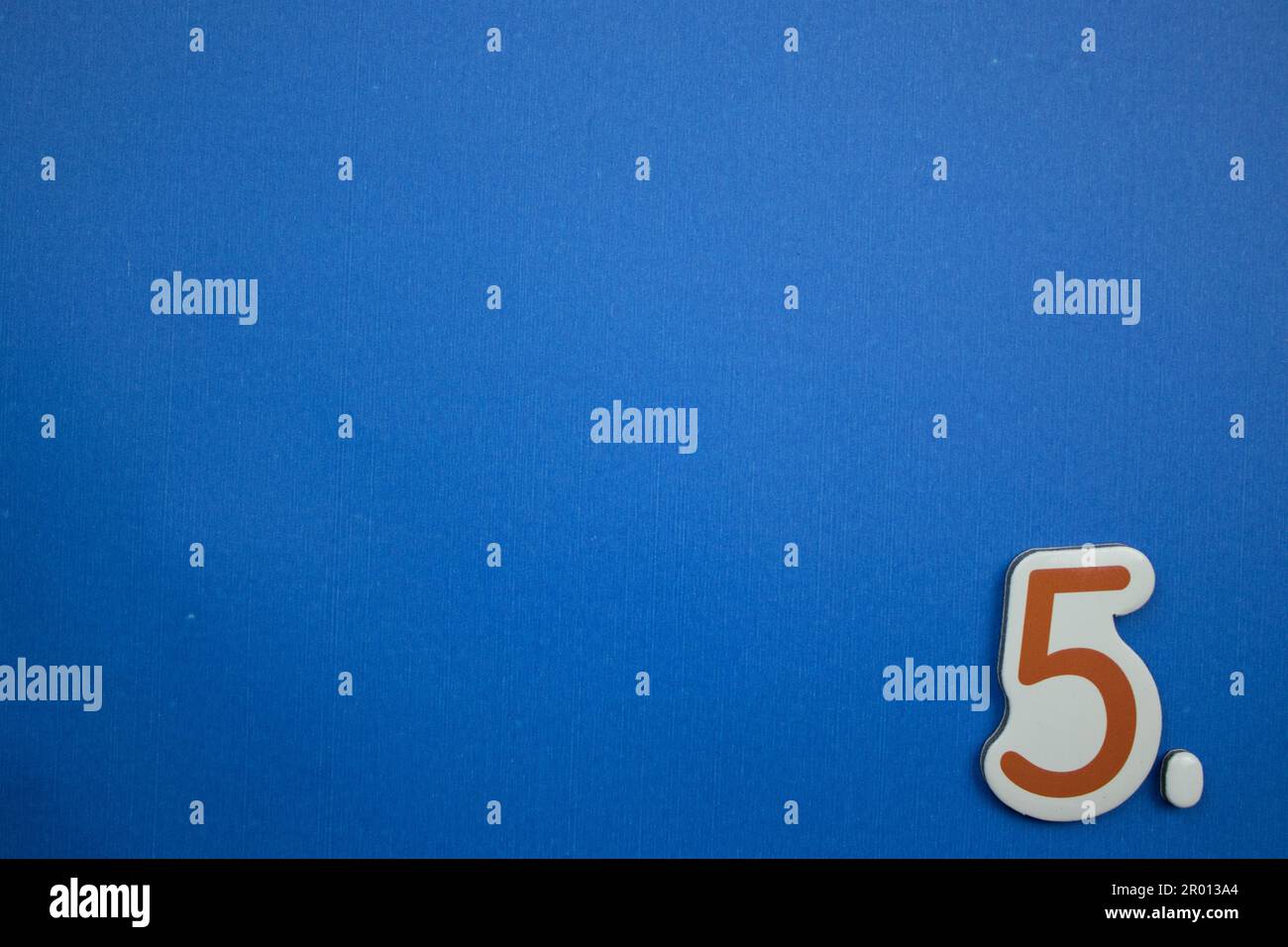 The number 5, orange and white, photographed from above, placed on the edge of a blue background. Stock Photo