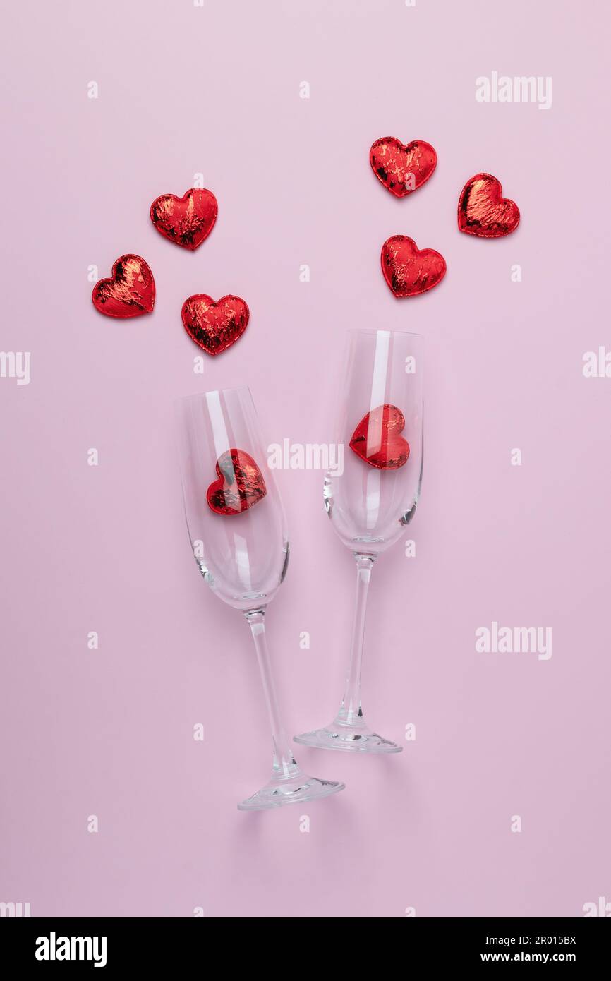 Romantic valentine postcard with two clinking champagne glasses with splash of red heart shaped confetti over pink background. Overhead, top view. Fla Stock Photo