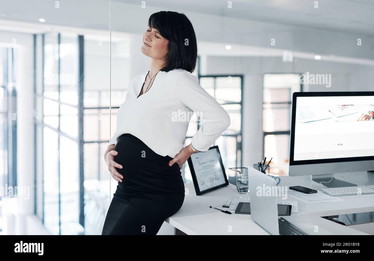 Someone wont let mommy work today. an attractive pregnant businesswoman standing alone in the office and suffering from abdominal pain. Stock Photo