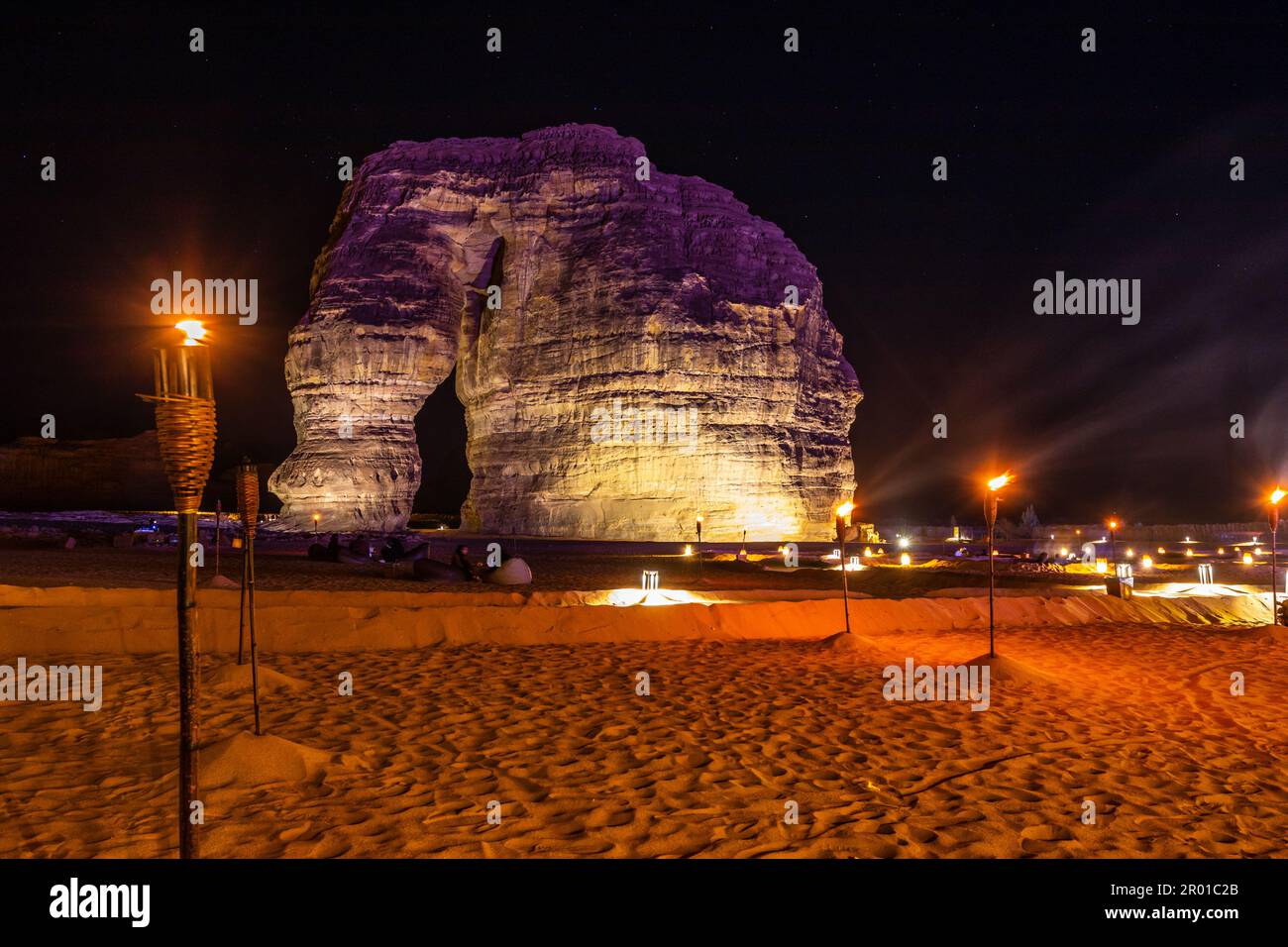 Illuminated by burning torches sandstone elephant rock erosion monolith standing in the night desert, Al Ula, Saudi Arabia Stock Photo