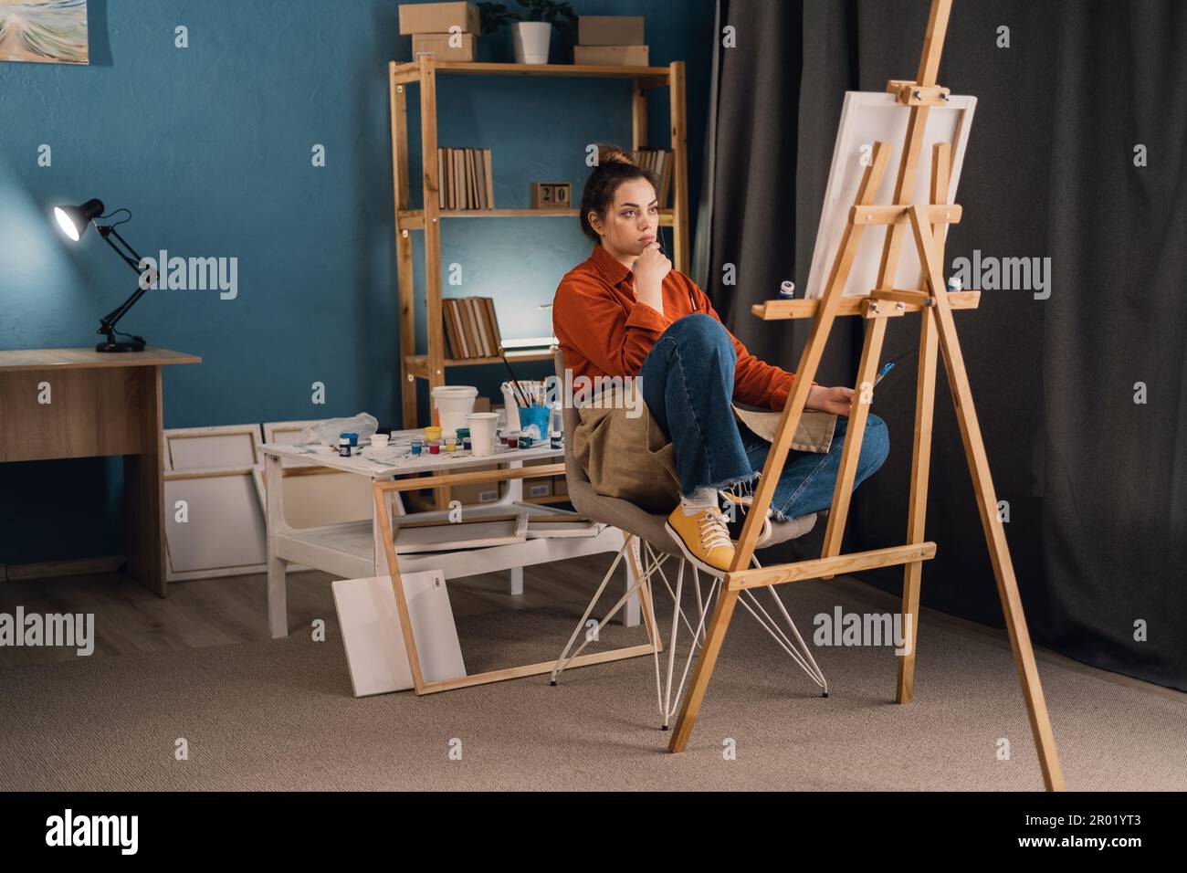 young brazilian woman artist in home studio sits on a chair near an ...