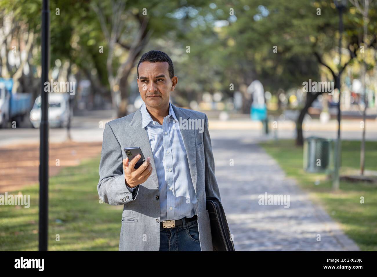 Young latin man in suit walking with mobile phone in hand. Stock Photo