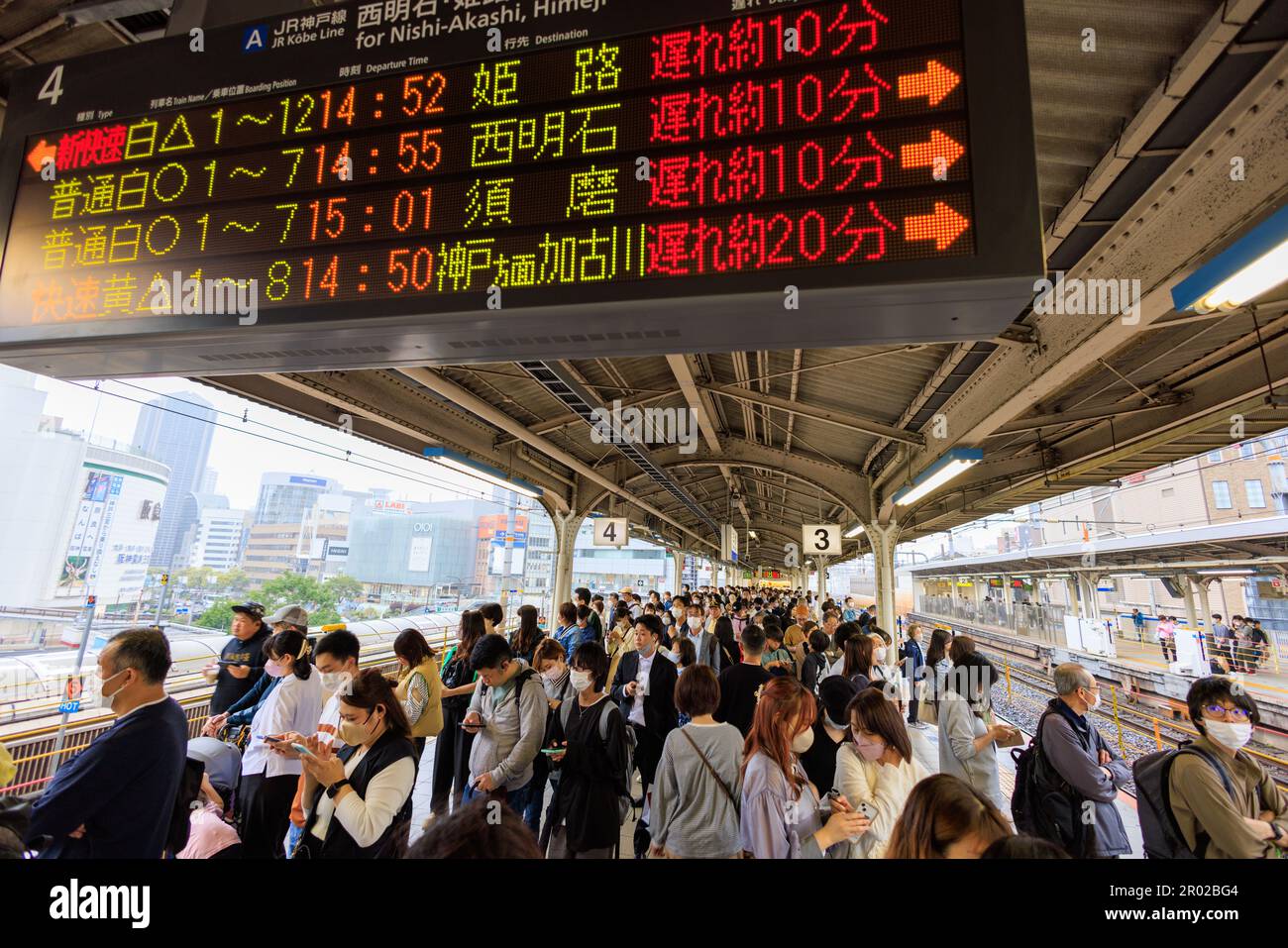 Kobe, Japan - May 6, 2023: Passengers wait on platform under sign with train delays at JR Sannomiya Station during Golden Week Holiday Stock Photo