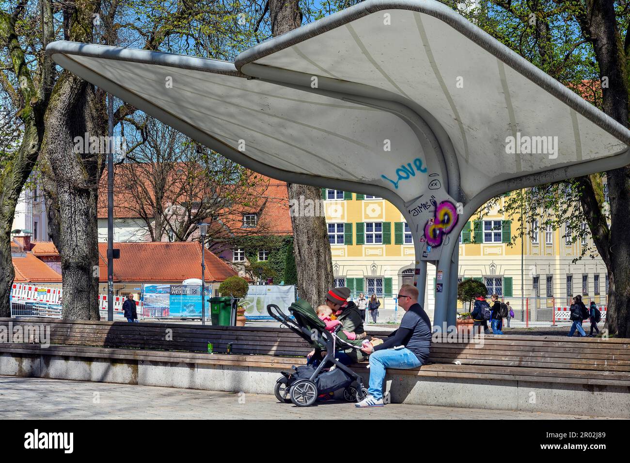 Rain and sun protection over park bench and parents with pram, Kempten, Allgaeu, Bavaria, Germany Stock Photo