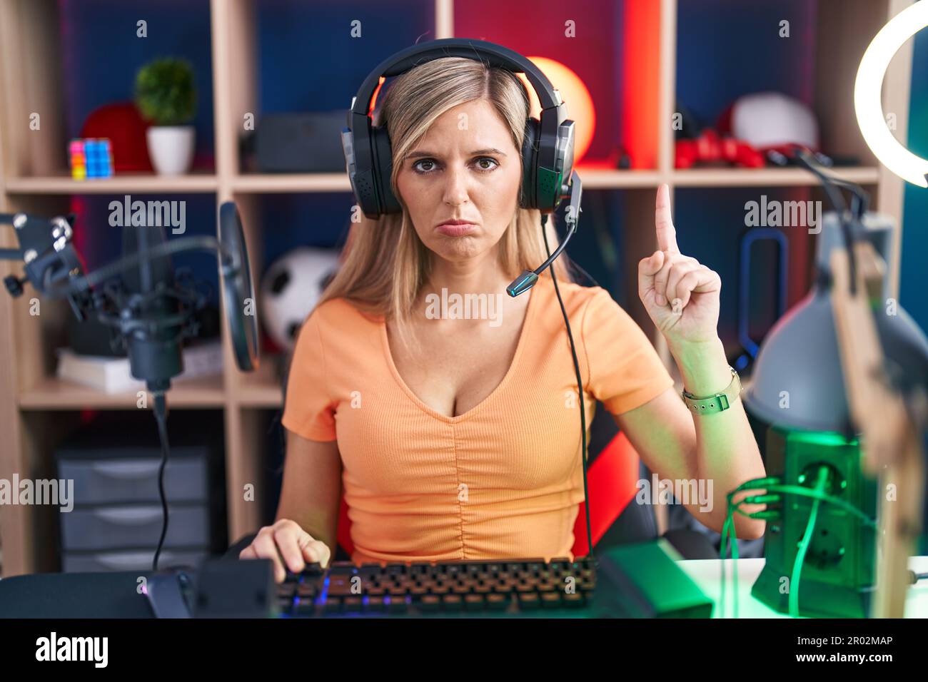 Young woman playing video games pointing up looking sad and upset ...