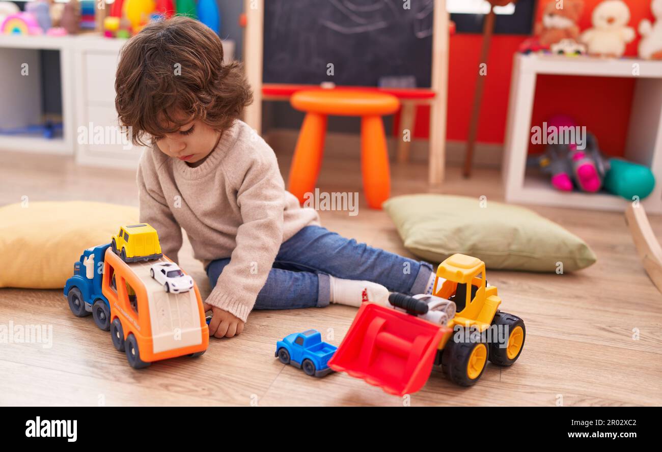 Adorable hispanic boy playing with car toy sitting on floor at ...