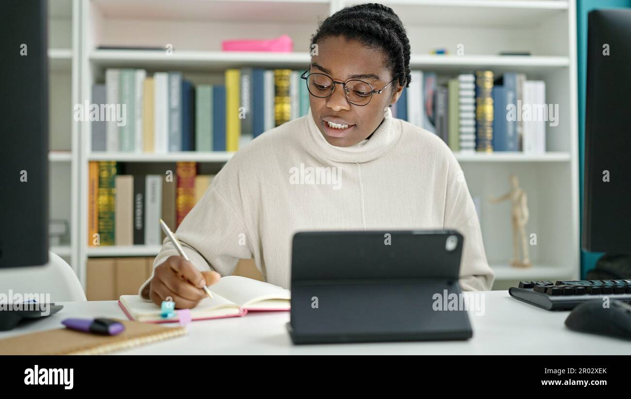 African american woman student using touchpad writing notes at library ...
