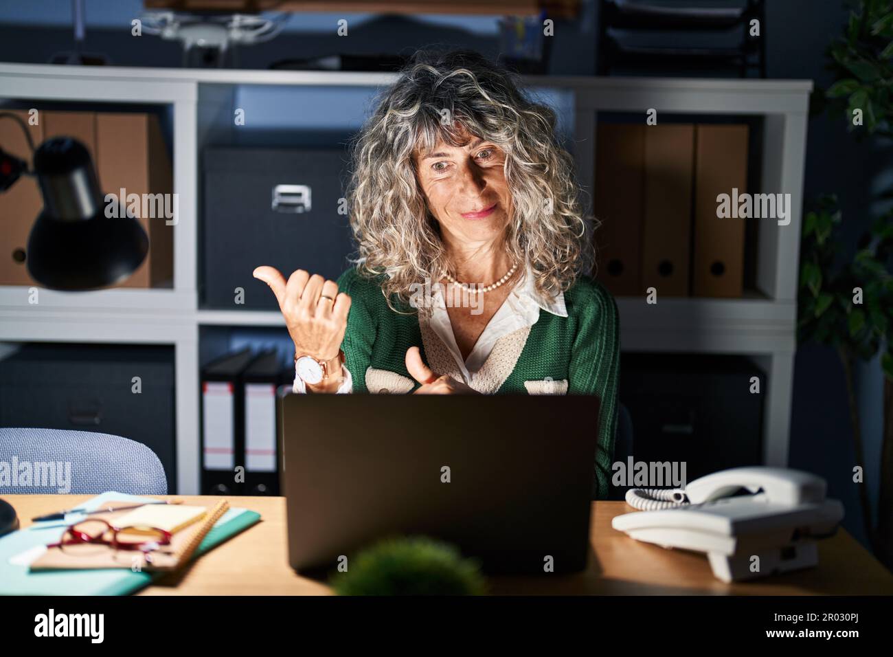 Middle age woman working at night using computer laptop pointing to the ...