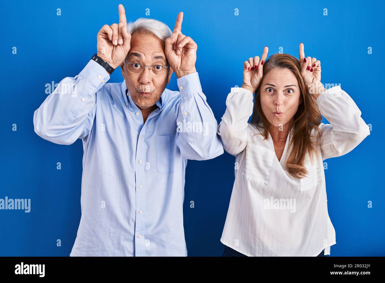 Middle age hispanic couple standing over blue background doing funny ...