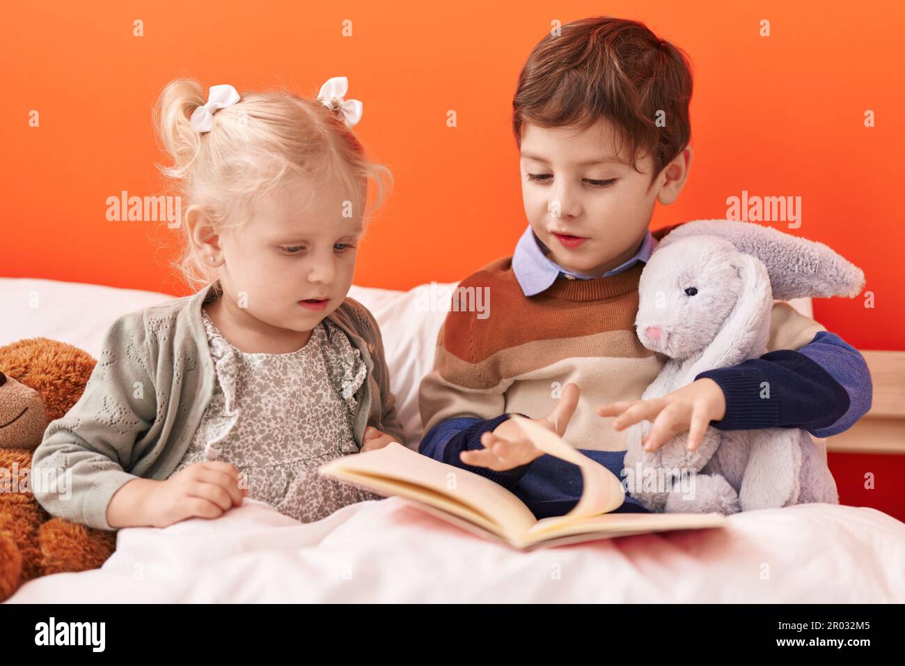Adorable boy and girl reading book sitting on bed at bedroom Stock ...