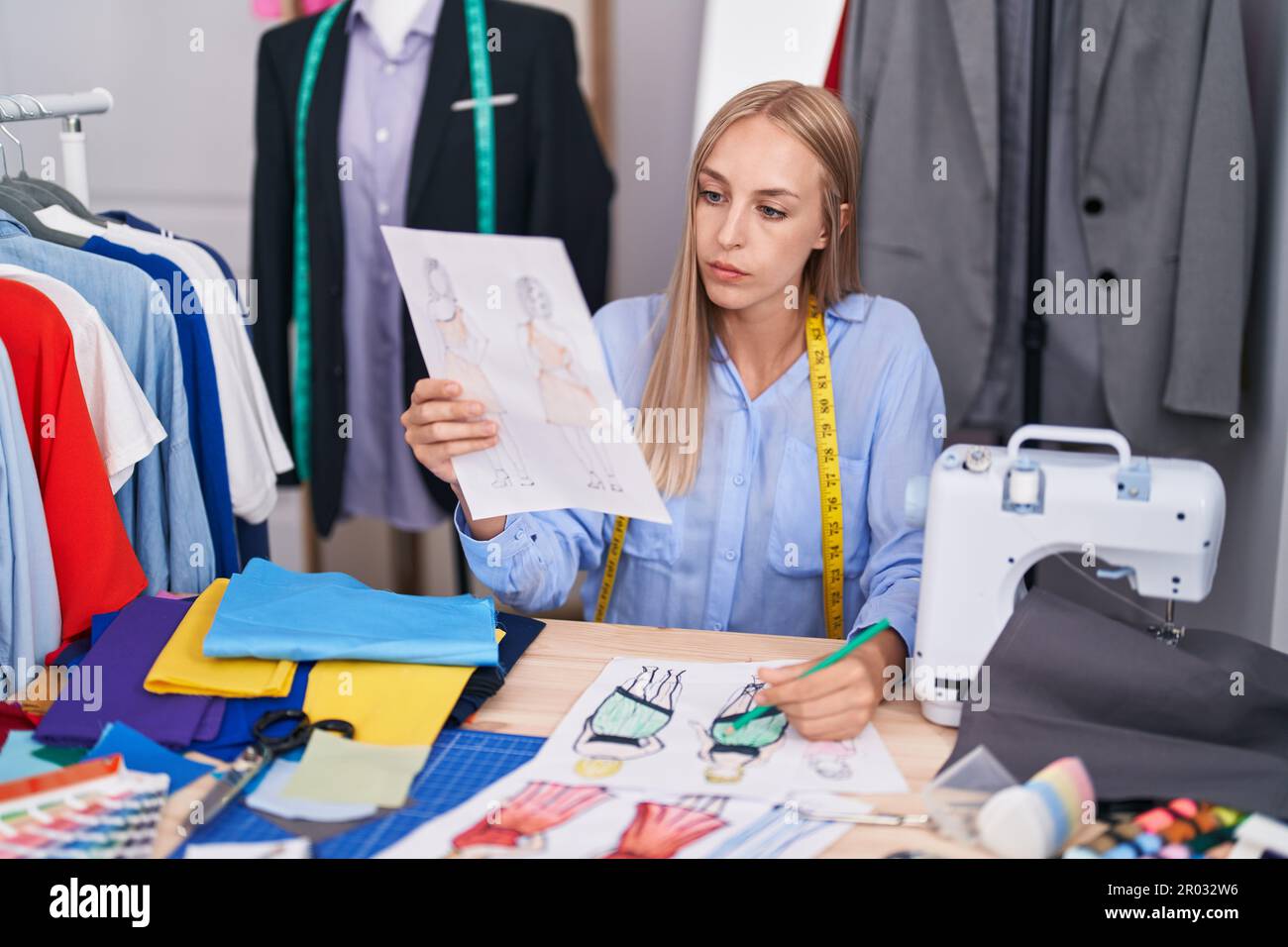 Young blonde woman tailor drawing clothing design at tailor shop Stock ...