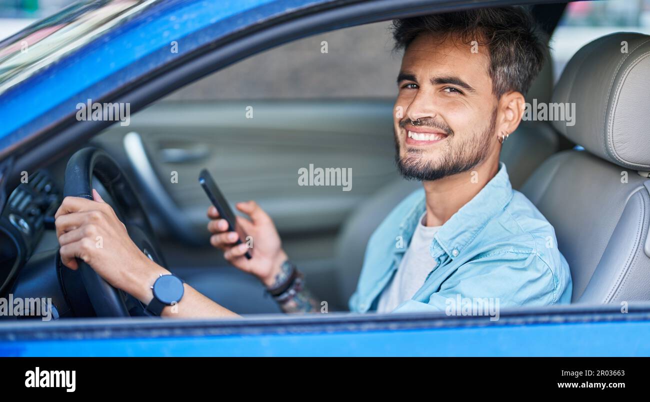 Young hispanic man using smartphone sitting on car at street Stock Photo