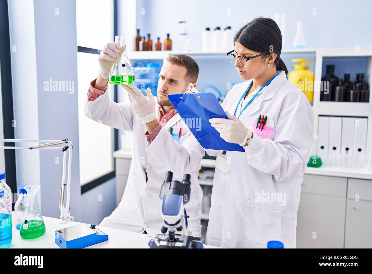 Man and woman wearing scientists uniform measuring liquid at laboratory ...