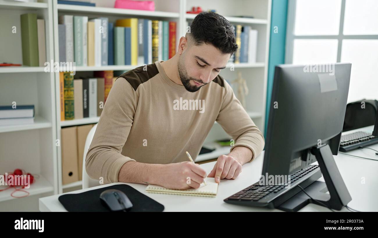 Young arab man student using computer writing on notebook at university ...