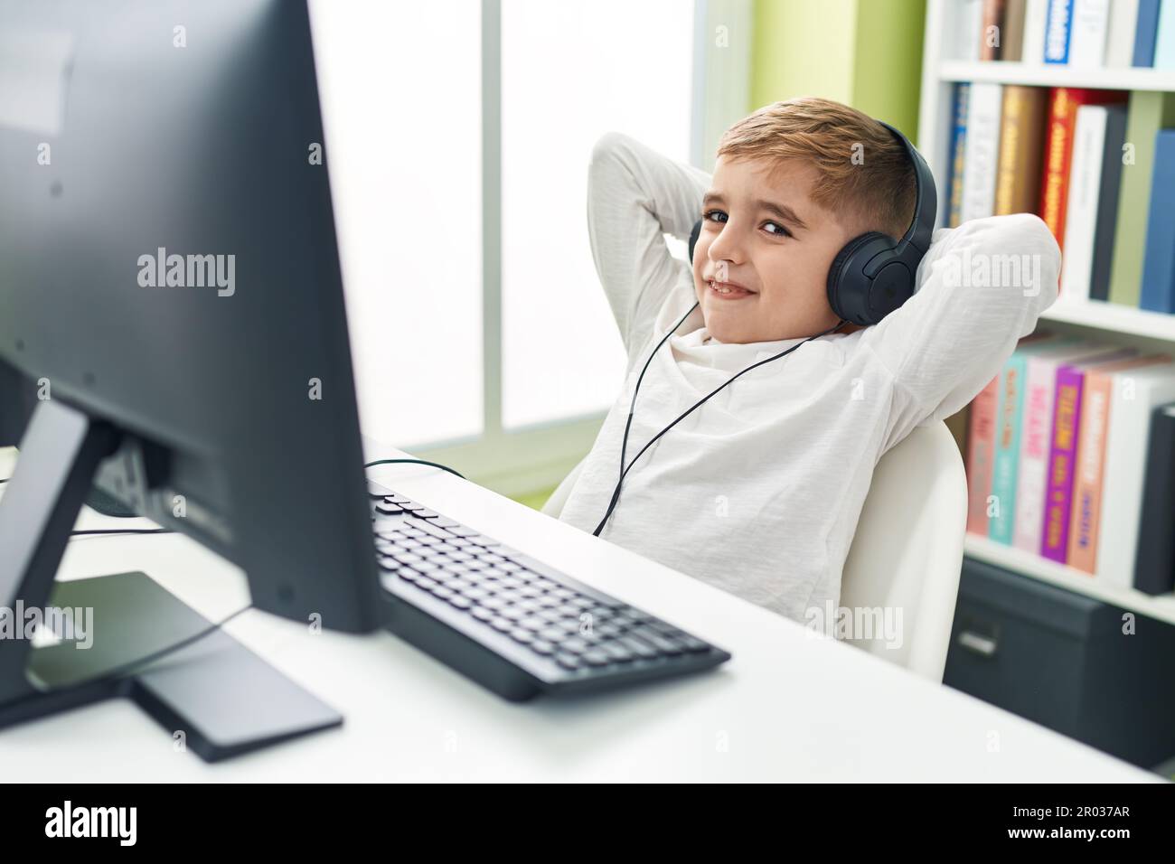 Adorable hispanic boy student using computer and headphones relaxing ...