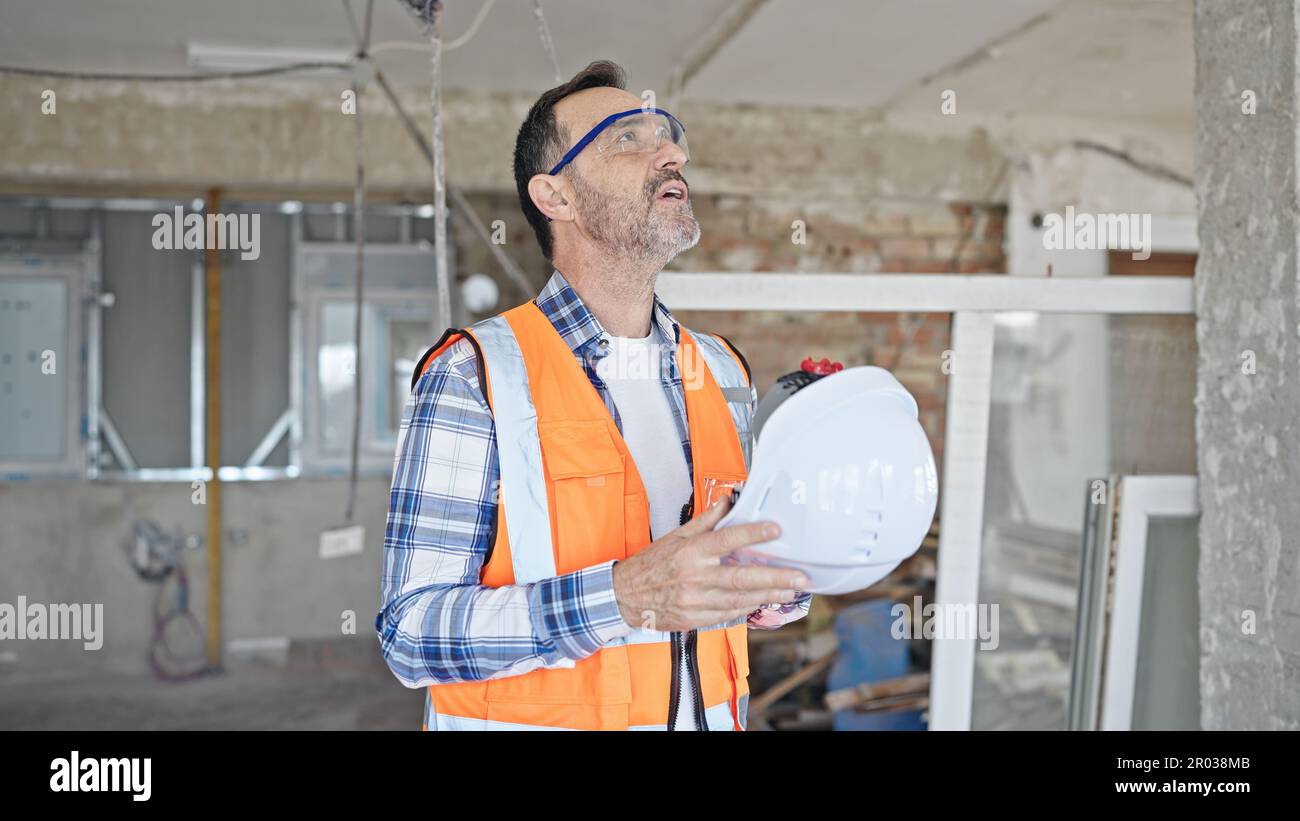 Middle age man builder tired using hardhat as a hand fan at construction site Stock Photo