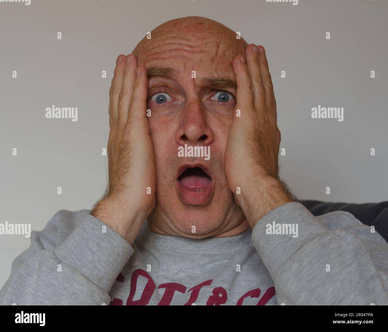 Portrait of scared worried man with hands on face, isolated on white background, bald male, blue eyes Stock Photo