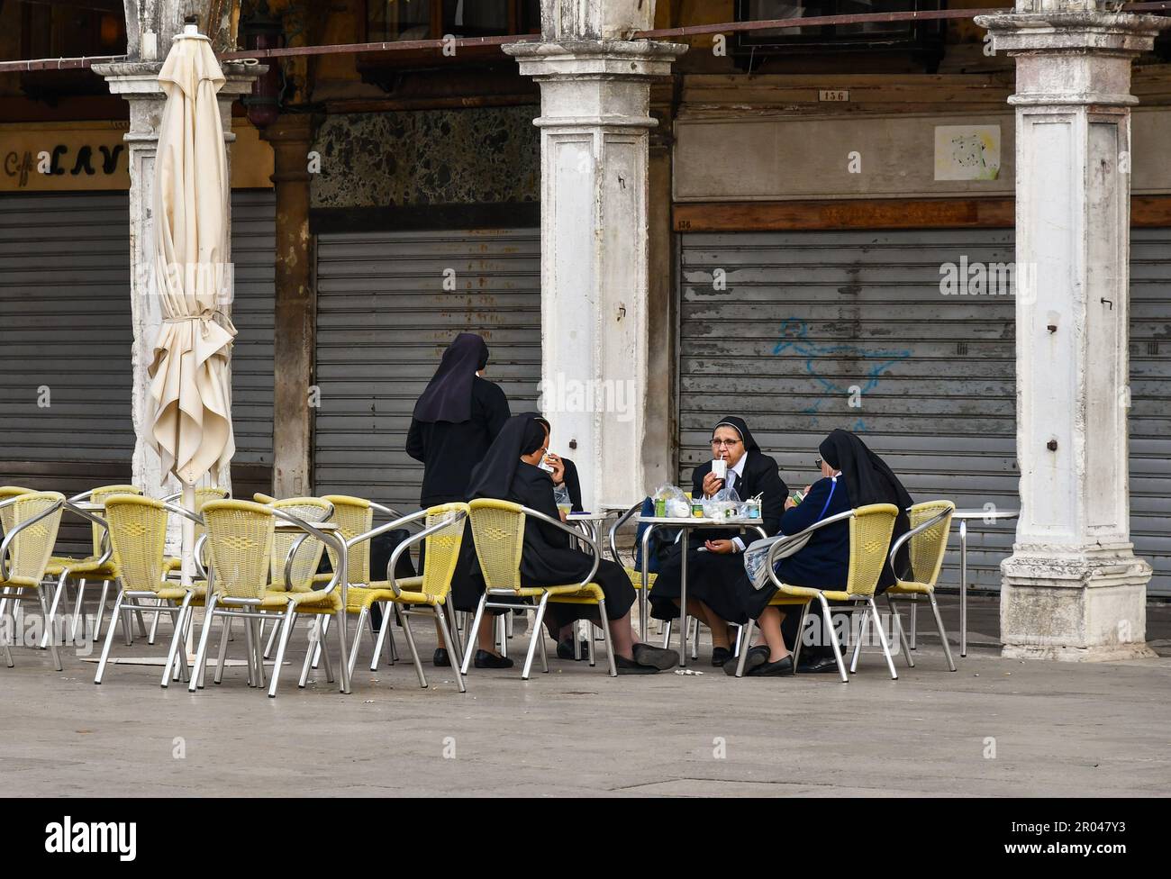 Small group of nuns rests at closed Caffè Lavena at the Procuratie Vecchie arcade in St Mark's Square, Venice, Veneto, Italy Stock Photo