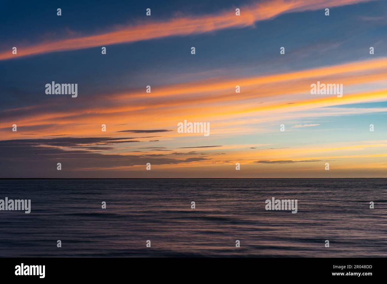 A calm body of water reflects a stunning sunset sky with beautiful ...