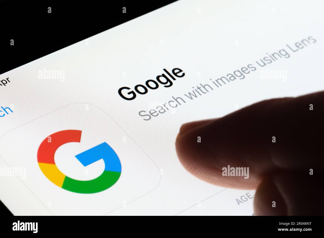 Google search app seen in App Store on the screen of ipad and blurred finger pointing at it. Selective focus. Stafford, United Kingdom, May 6, 2023 Stock Photo