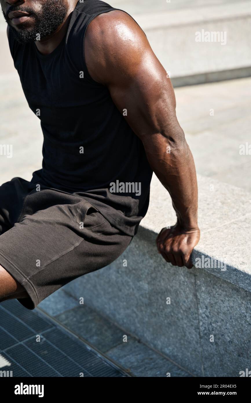 Fit young African man wearing black sportswear training in urban park. Stock Photo