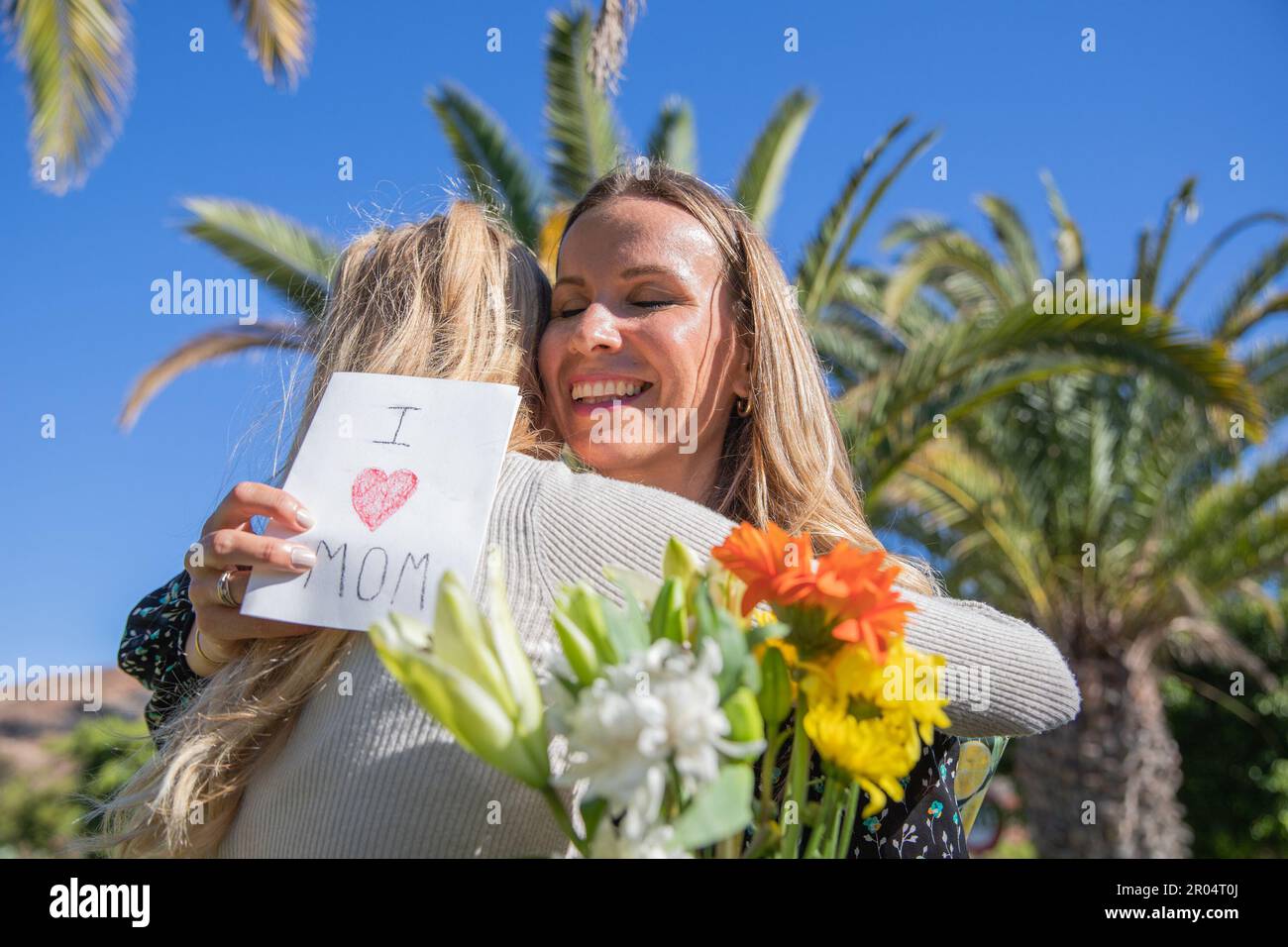 Smiling mother hugs her daughter who celebrates her on mother's day with a card and flowers Stock Photo