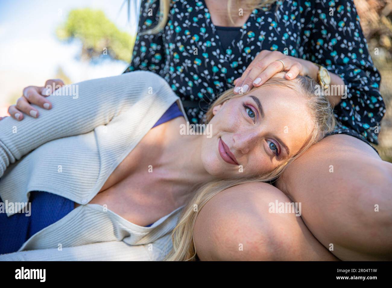 Portrait of a girl resting her head on the legs of her mother who cuddles and protects her Stock Photo