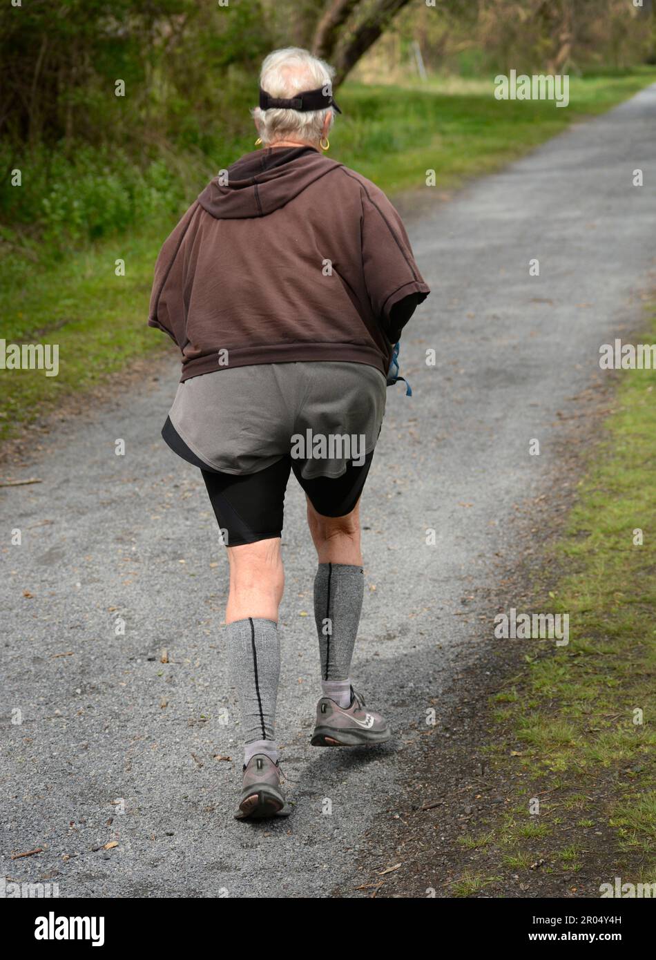 A senior woman jogs along the public Virginia Creeper trail in Abingdon, Virginia. Stock Photo