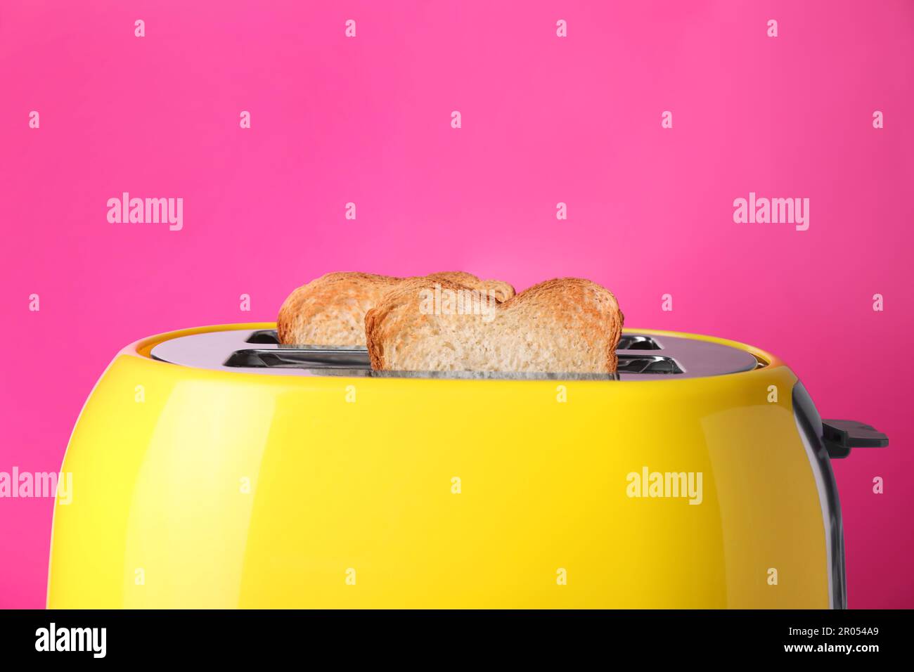 Yellow toaster with roasted bread against pink background, closeup