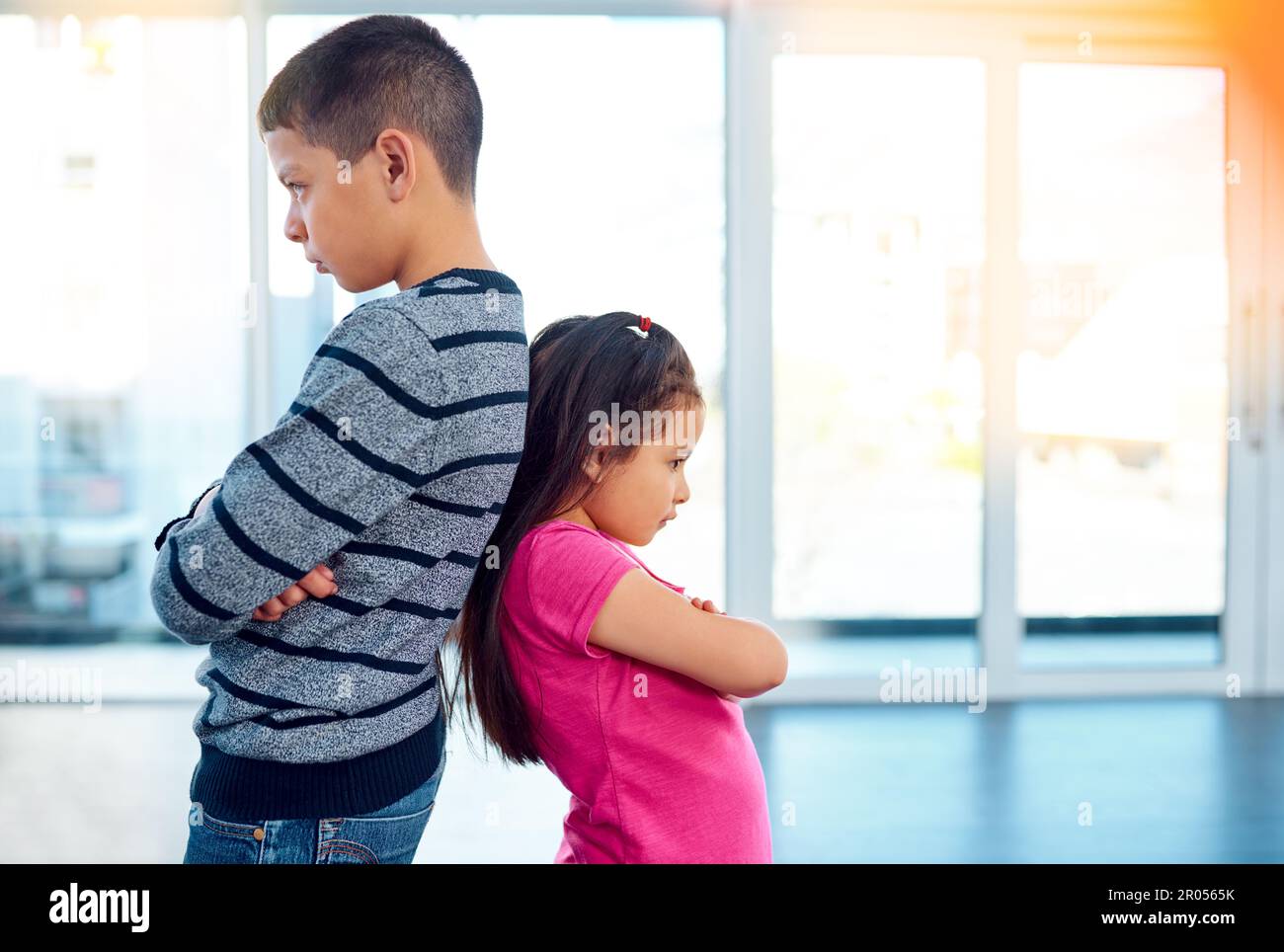 I wonder who started it this time. Shot two naughty young children posing with their arms folded and backs facing each other at home. Stock Photo