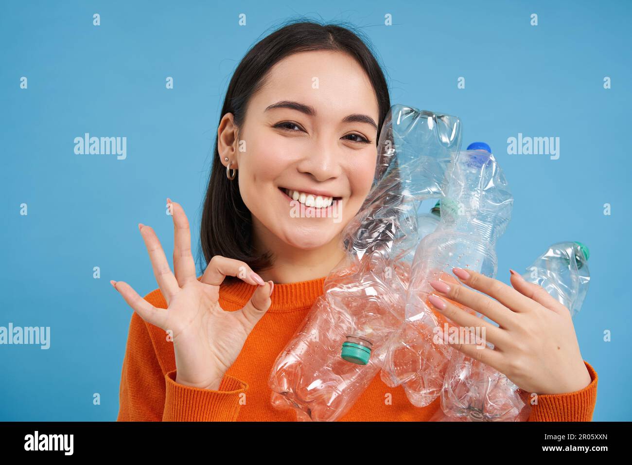 Recycling is great. Smiling young woman, holding bottles, shows okay ...