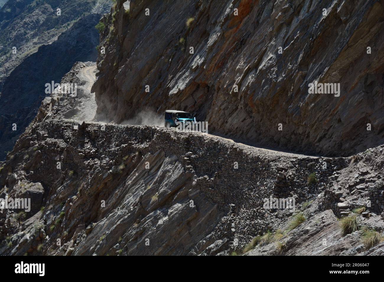 A sturdy jeep navigates a treacherous road, carved between towering mountains in Pakistan Stock Photo