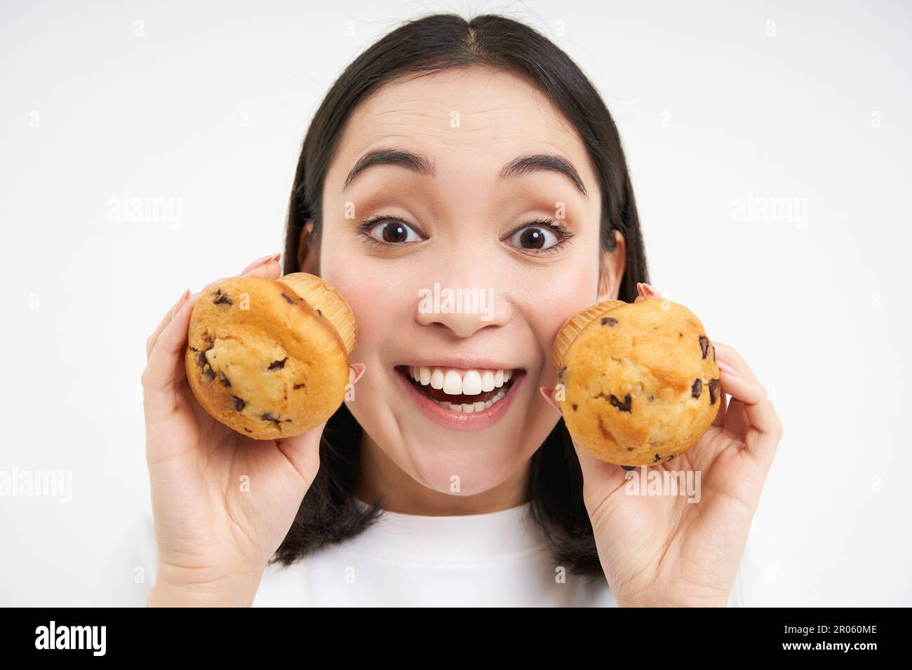 Close Up Portrait Of Asian Woman Shows Two Cupcakes Near Face And Smiles Likes Pastry Enjoys 