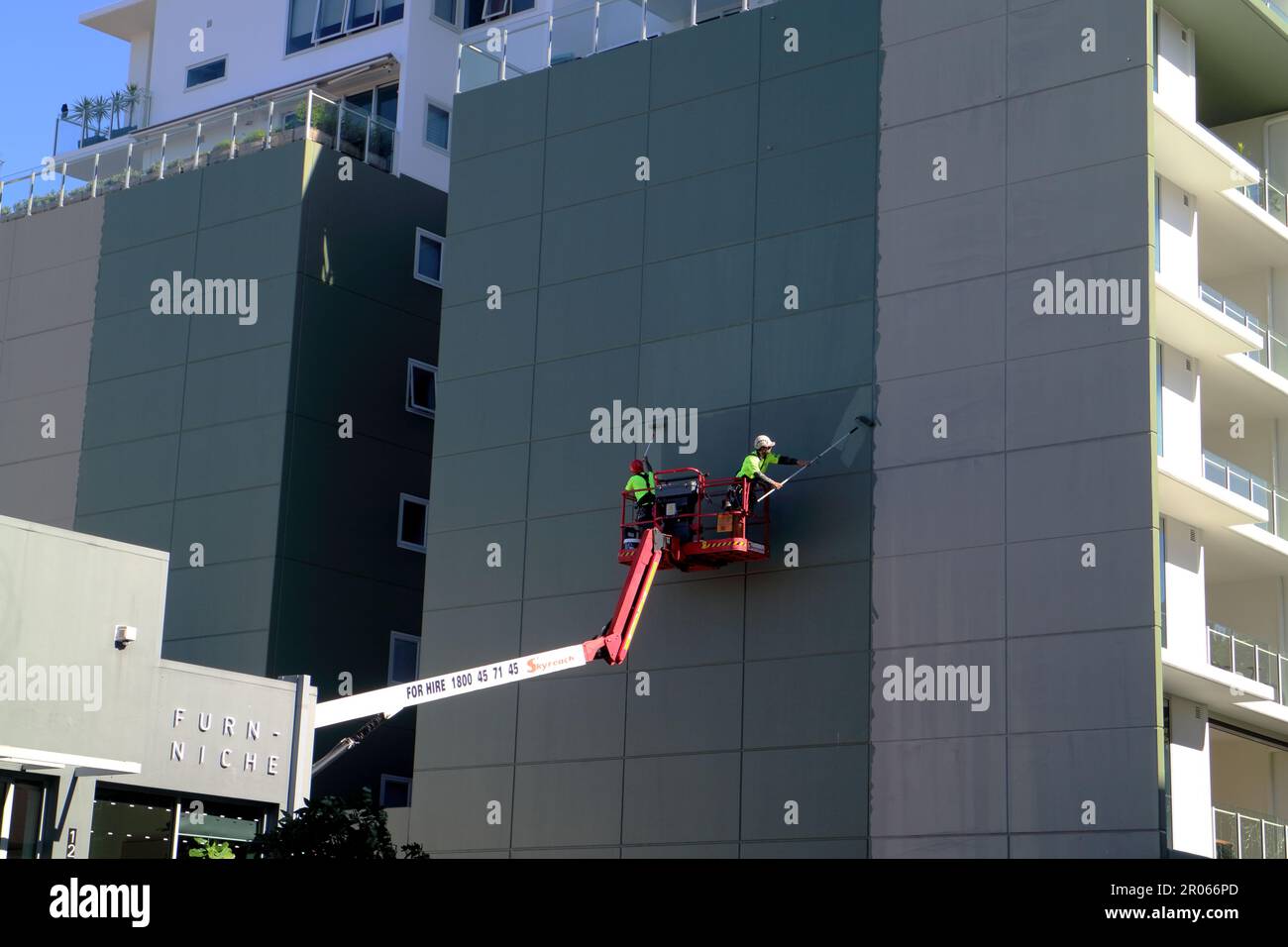 Two people painting an apartment building wall using a crane Stock