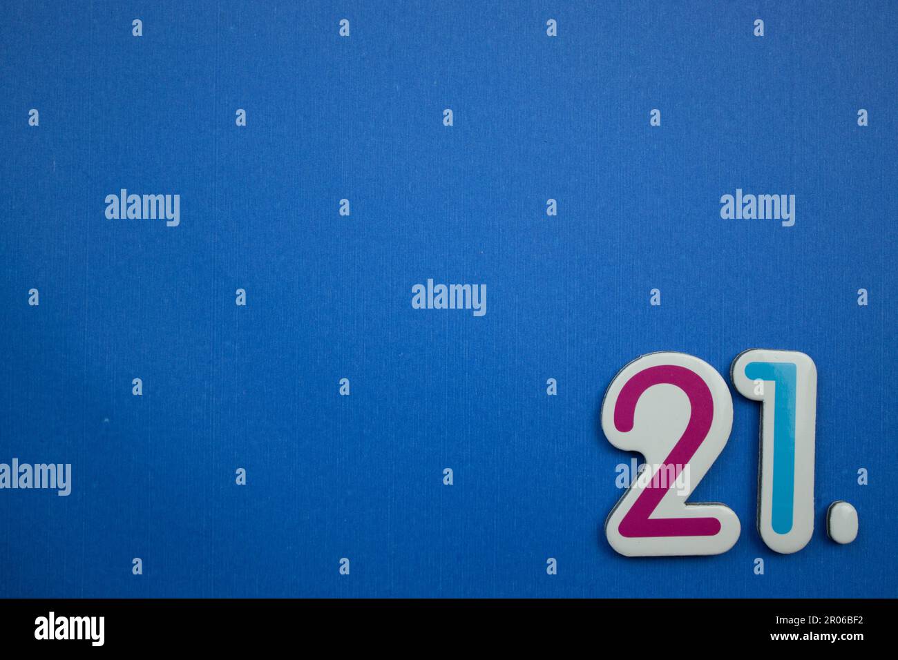 The number 21, placed on the edge of a blue background, photographed from above, colored red and light blue. Stock Photo