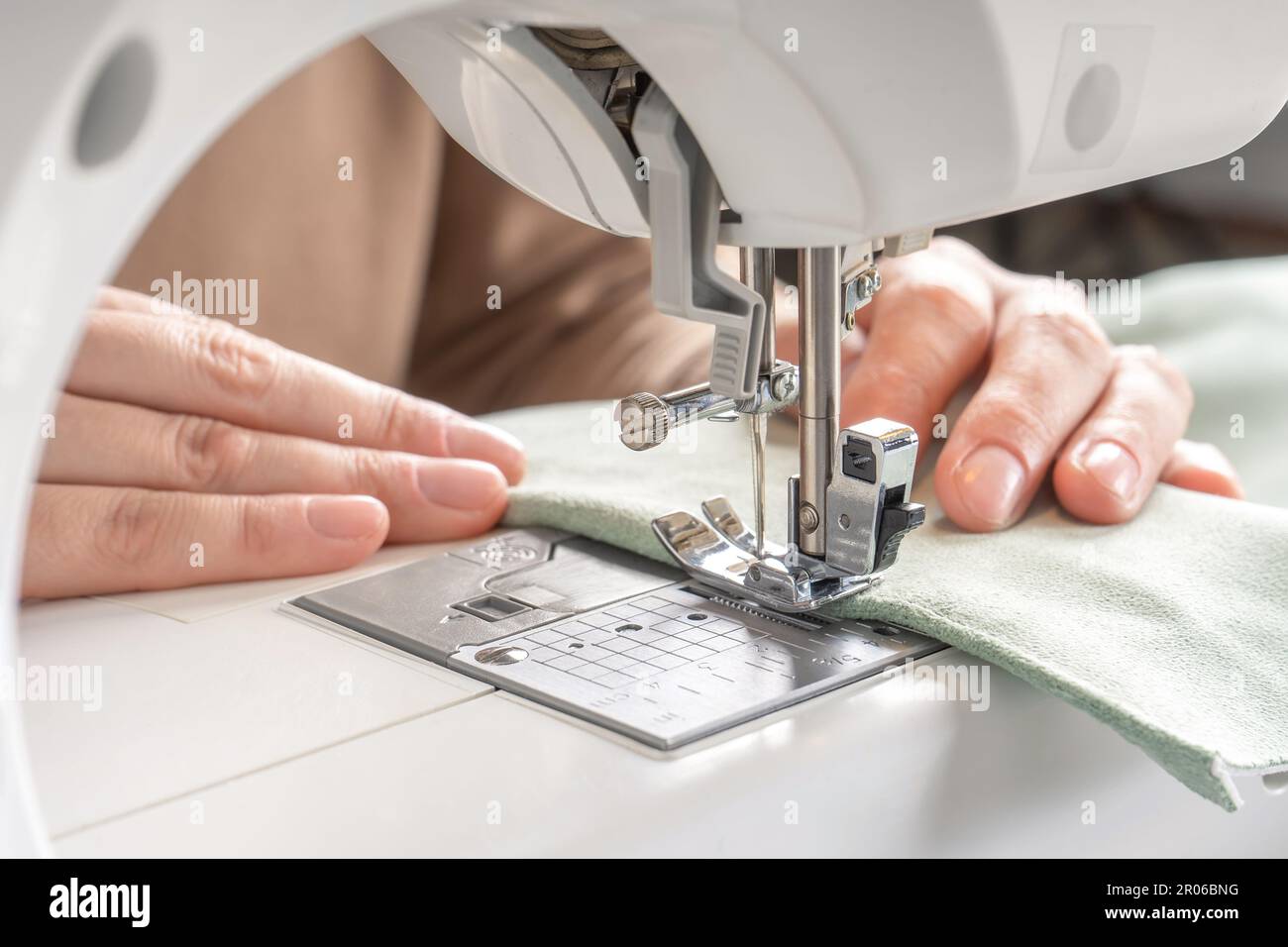 Female hands stitching white fabric on modern sewing machine at workplace in atelier. Women's hands sew pieces of fabric on a sewing machine close-up. Stock Photo