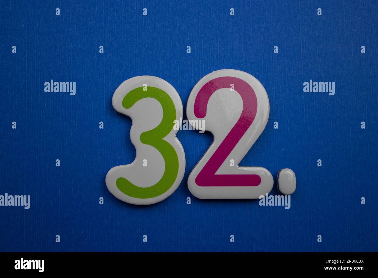 The number 32, placed on a blue background, photographed from above, colored green and red. Stock Photo