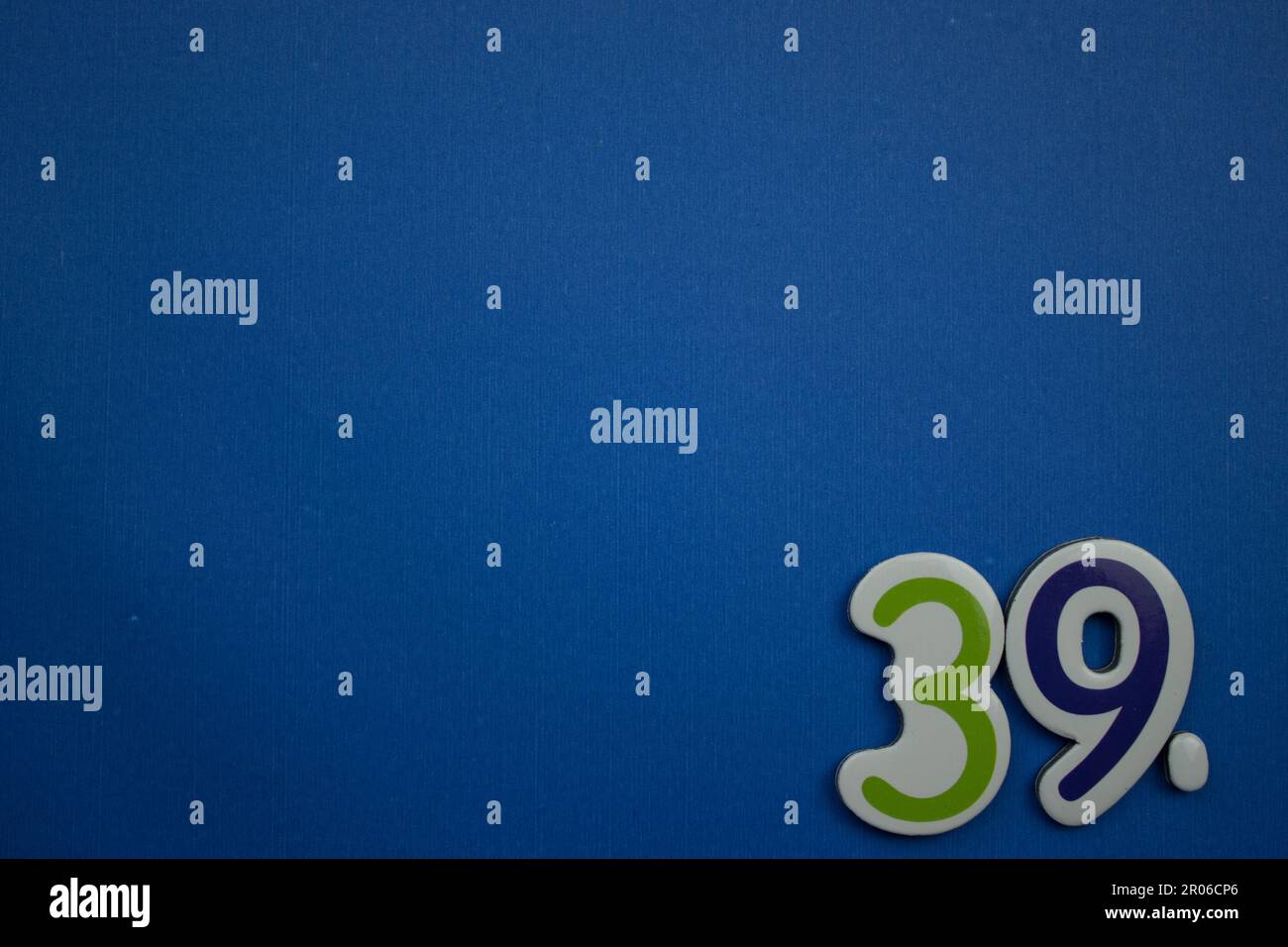 The number 39, placed on the edge of a blue background, photographed from above, colored green and dark blue. Stock Photo