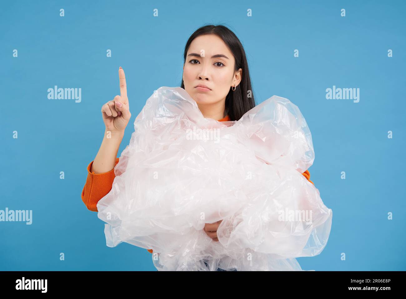 Asian woman with plastic bags, recycling waste in hands, points up