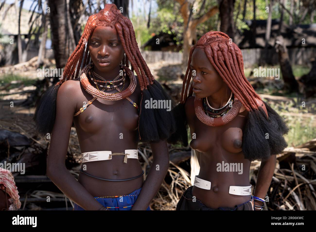 Himba people in Namibia- Young women of the tribe with a typical outfit stand bare chested Stock Photo