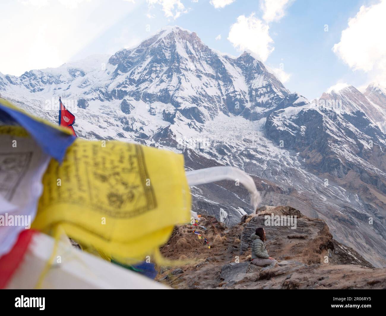 Prayer flags and female  sitting in Annapurna Base camp doing a meditation to thank the spirits of nature after all the effort that took to get there. Stock Photo