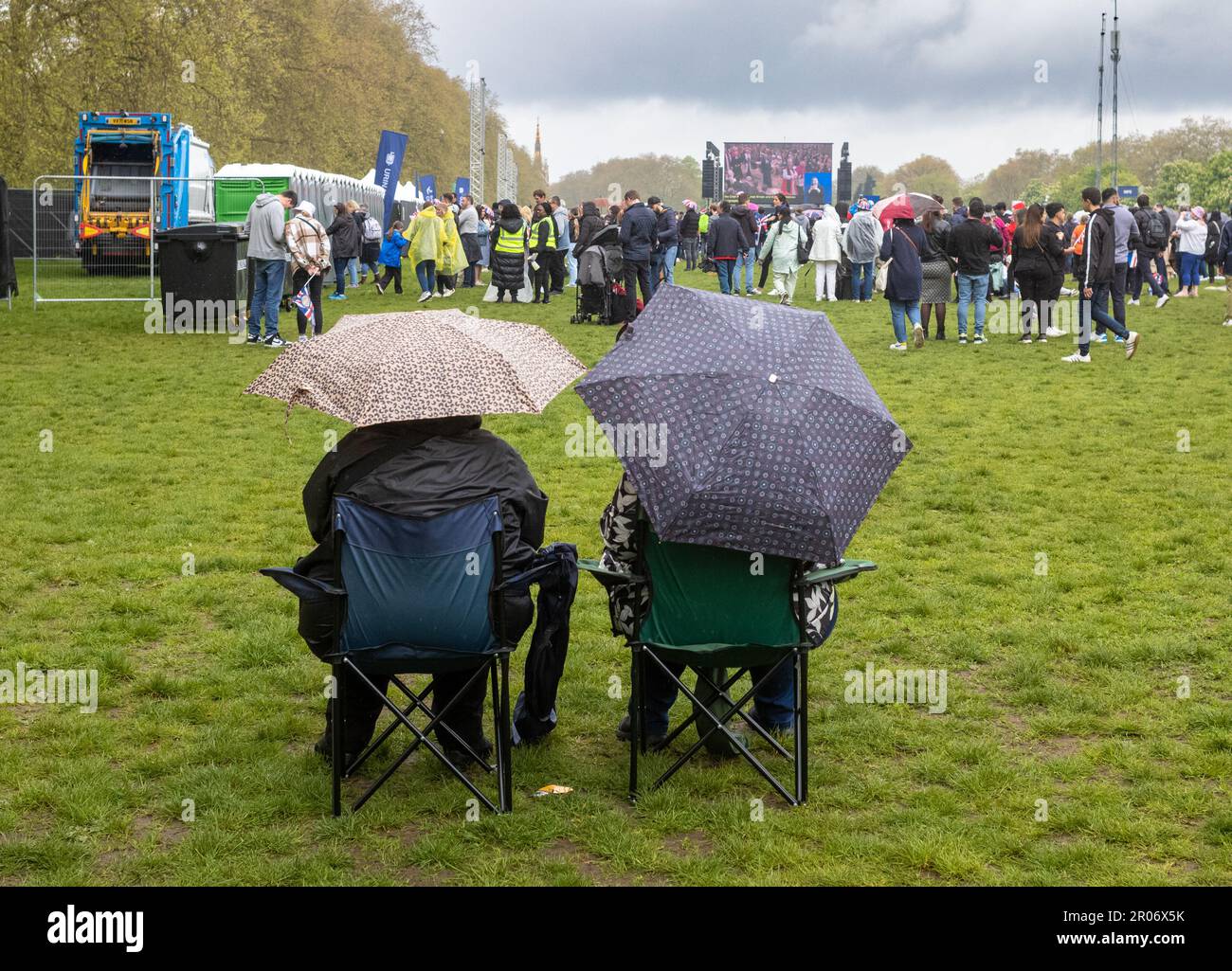 In the pouring rain, a couple sit on folding chairs under umbrellas to