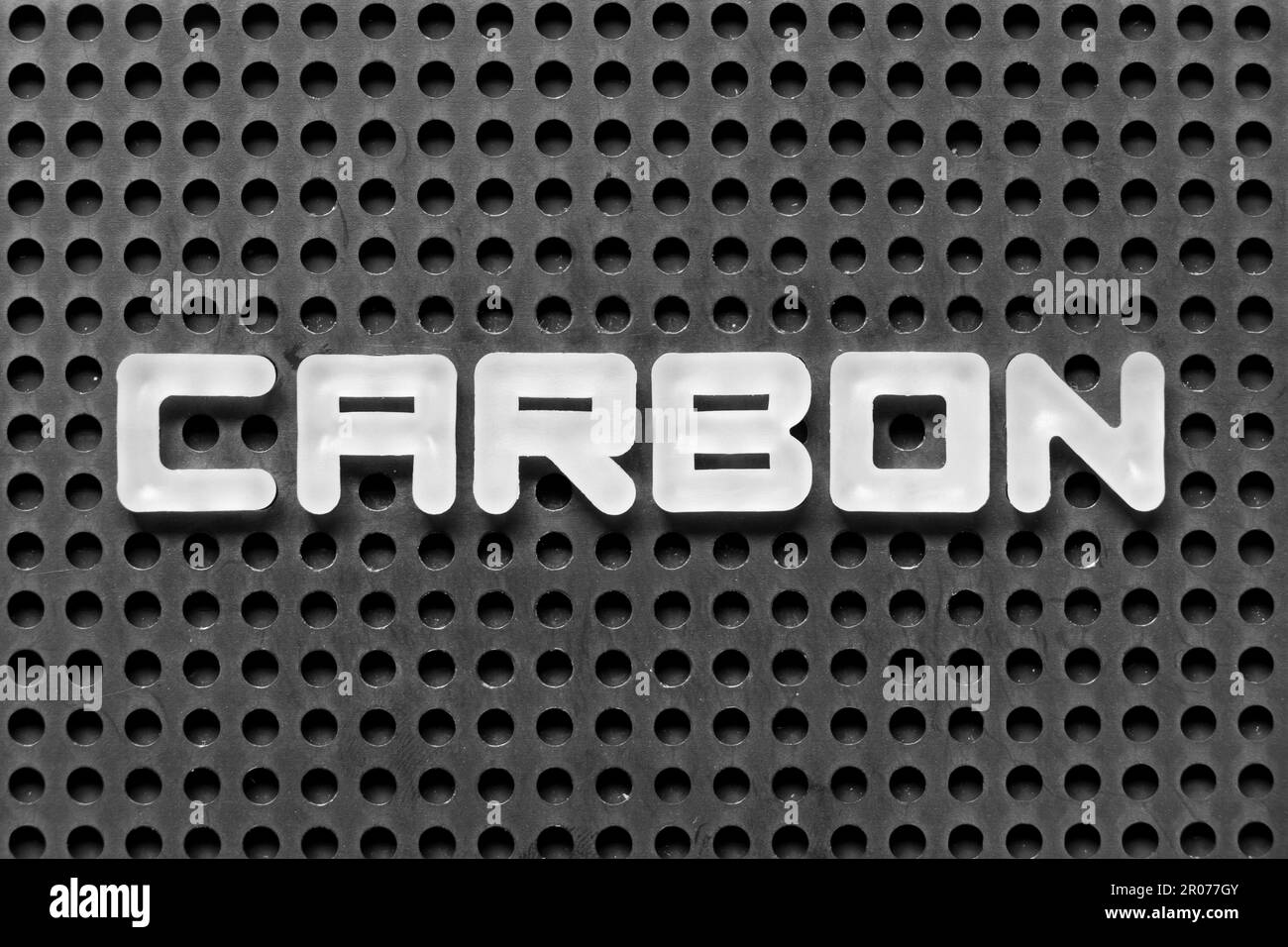 White alphabet letter in word carbon on black pegboard background Stock